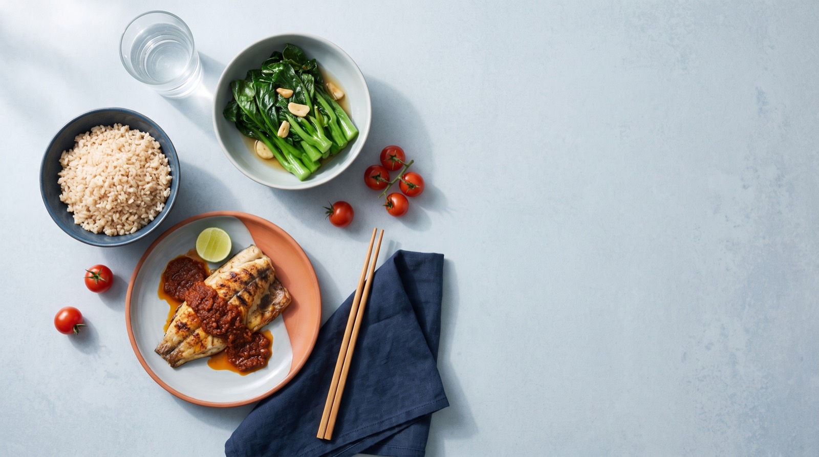 A balanced meal of brown rice, steamed greens and grilled fish with a glass of water