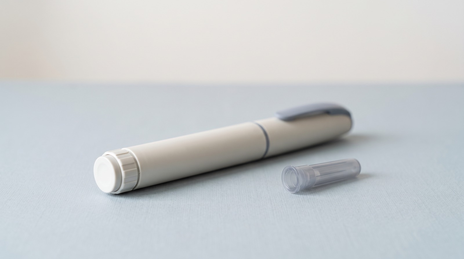A plain, unbranded injector pen with its cap removed, on a pale surface